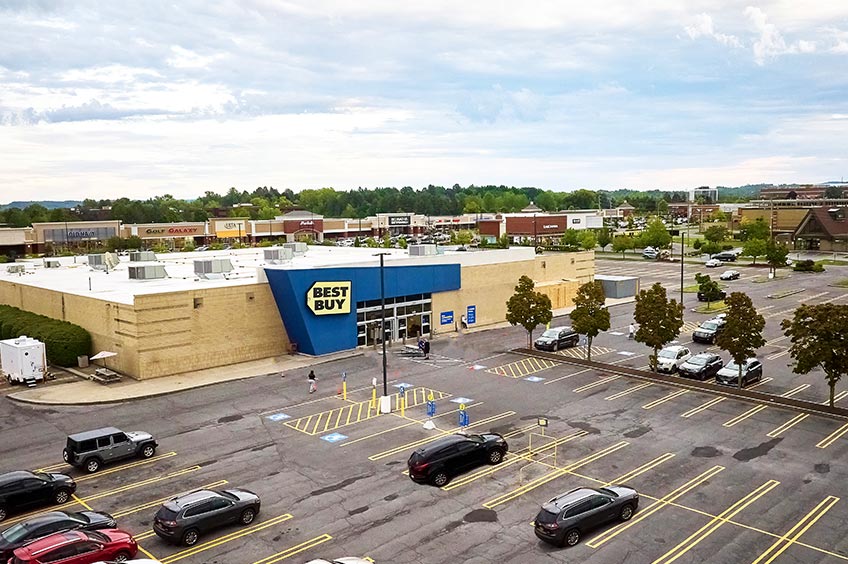 Overhead shot of Dewitt shopping center and its adjacent parking lot, captured from a high vantage point.