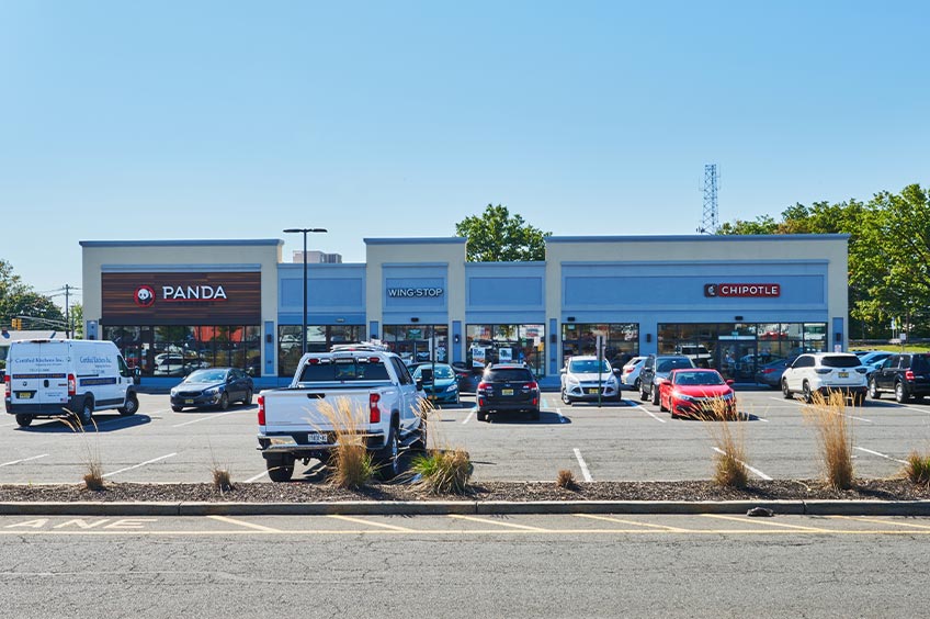 Image of Woodbridge Commons shopping center with various shops and parking spaces.